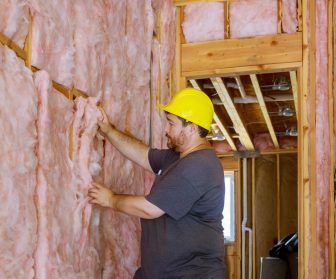 Man installing thermal insulation layer under the wall using mineral wool with fiberglass cold soft focus